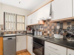 A modern kitchen with white cabinets, a black countertop, and a tiled backsplash.