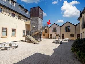Un patio con bancos de piedra, una escalera central y una torre con reloj.