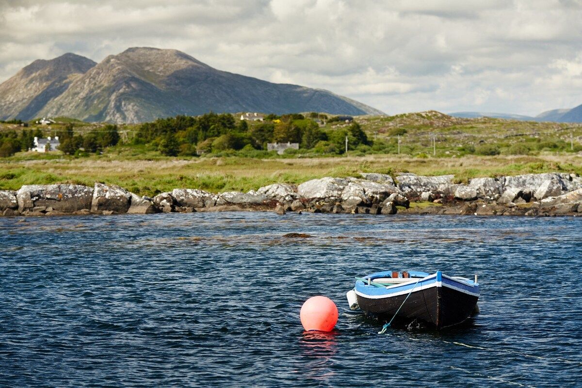 A boat on calm water with a rocky shoreline and mountains in the background.