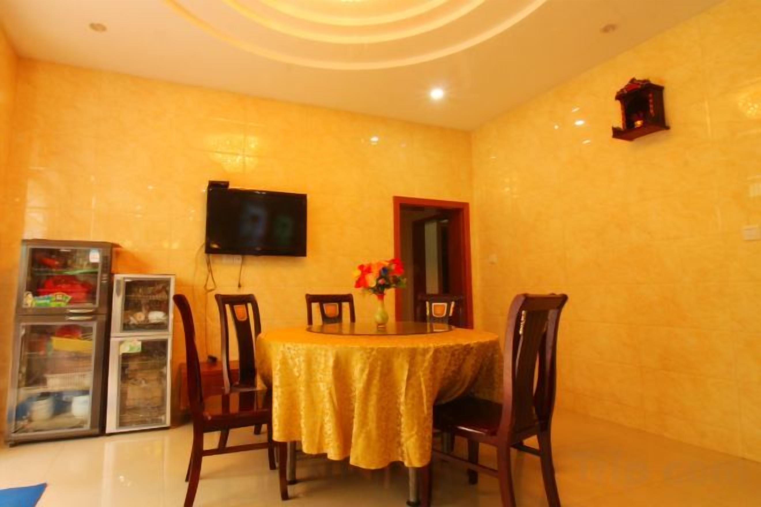 A dining area with a round table, chairs, a television mounted on the wall, and a refrigerator.