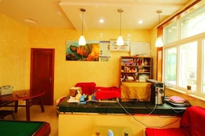 A room with a pool table, a red sofa, a small table with items, a bookshelf, and a window with daylight. - Jufangge Hotel (Shengsi)
