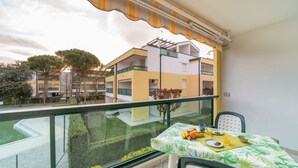 A balcony with a table set for breakfast, overlooking a building with a yellow facade and a green lawn.