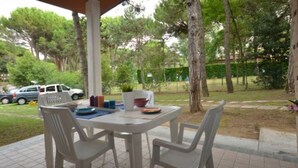 Eine Terrasse mit Tisch und Stühlen, umgeben von Bäumen und einem parkenden Auto.