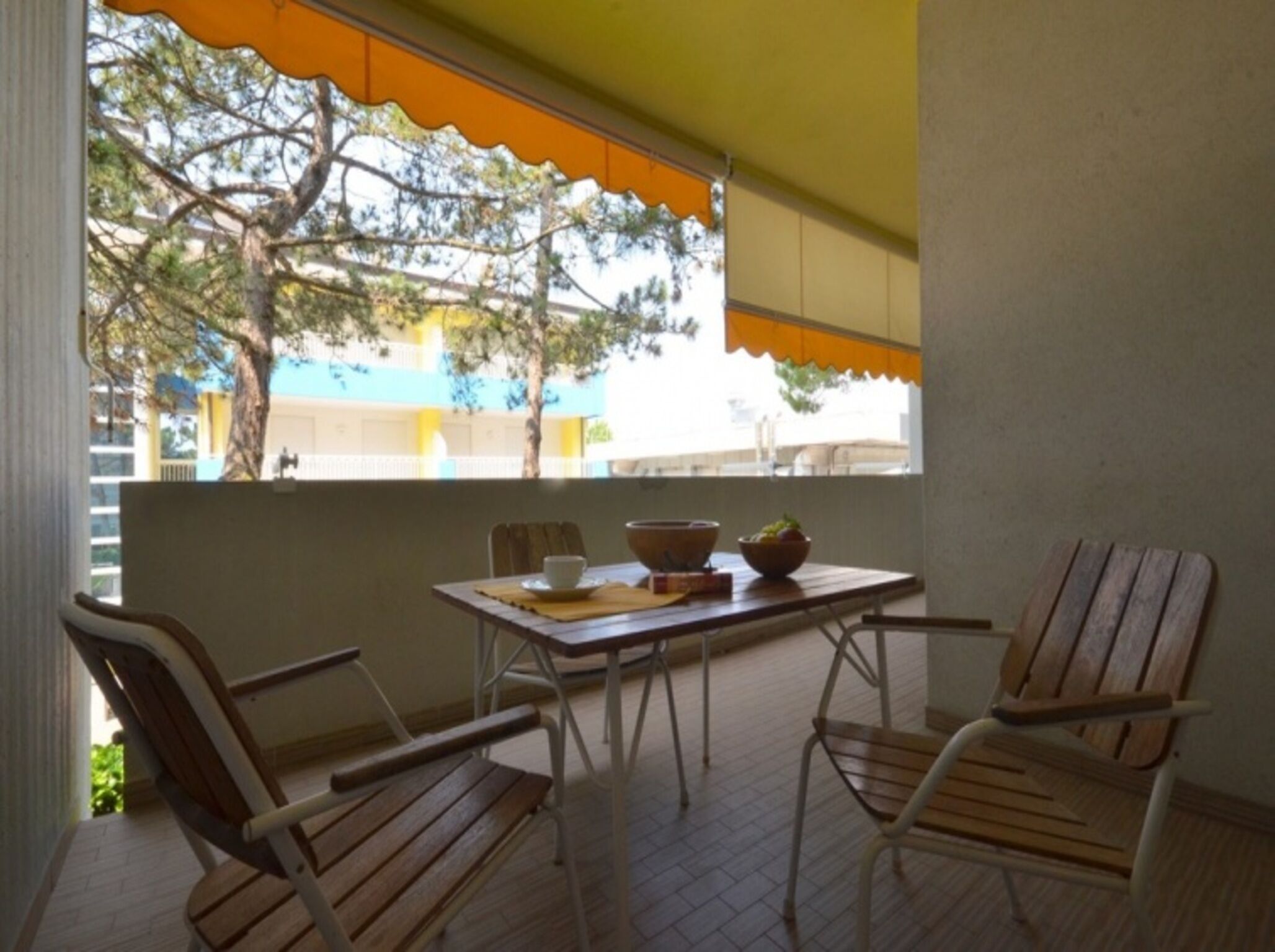 A balcony with a table, chairs, and a view of a tree and building.
