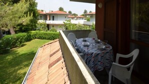Un balcón con mesa lista para comer, con vistas a un jardín cuidado y casas vecinas.