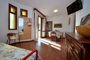 Une pièce comprenant un lit, une commode en bois, une table à manger avec des chaises, un téléviseur fixé au mur et une fenêtre avec des rideaux.