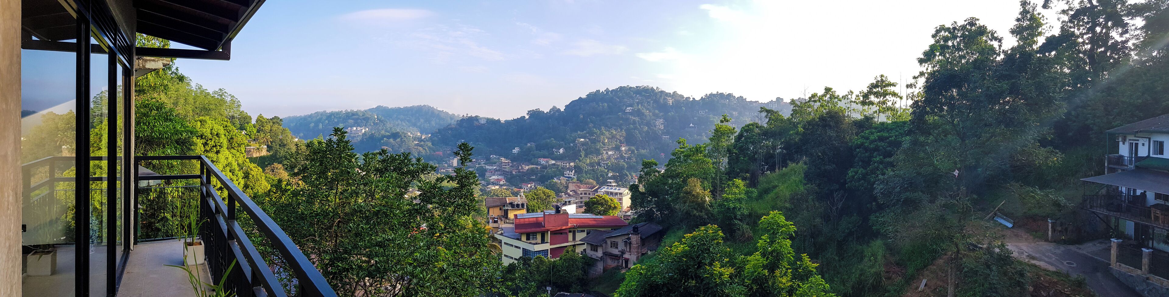 A view from a balcony overlooking a hillside with buildings and lush greenery.