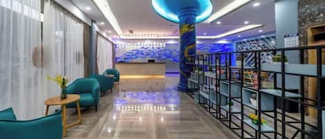 A hotel lobby with a reception desk, teal seating, and a decorative column.