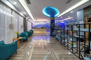 Eine Hotelhalle mit einer Rezeption, Sitzgelegenheiten in Türkis und einer dekorativen Säule.