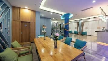 A modern hotel lobby with a wooden reception desk, green cushioned seating, and a staircase.