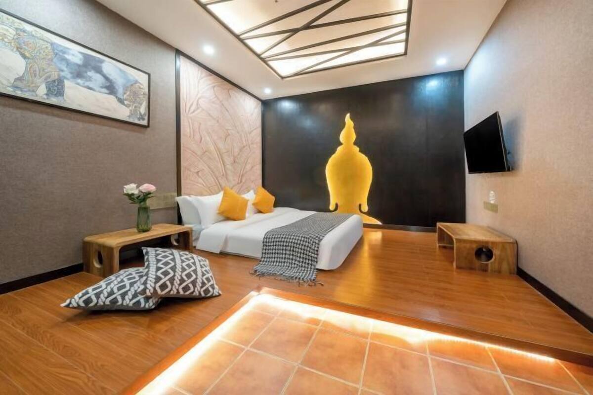 Ein modernes Hotelzimmer mit Bett, kleinem Tisch, Wand-Fernseher und einer dekorativen Wandarbeit.