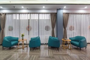 Una habitación con zona de estar que incluye dos sillas color turquesa y una pequeña mesa redonda, un ventanal con cortinas translúcidas y un suelo de madera pulida.