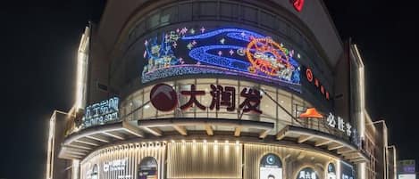 Un edificio grande e iluminado con una entrada circular y varios letreros, incluyendo uno que dice '大润发'.