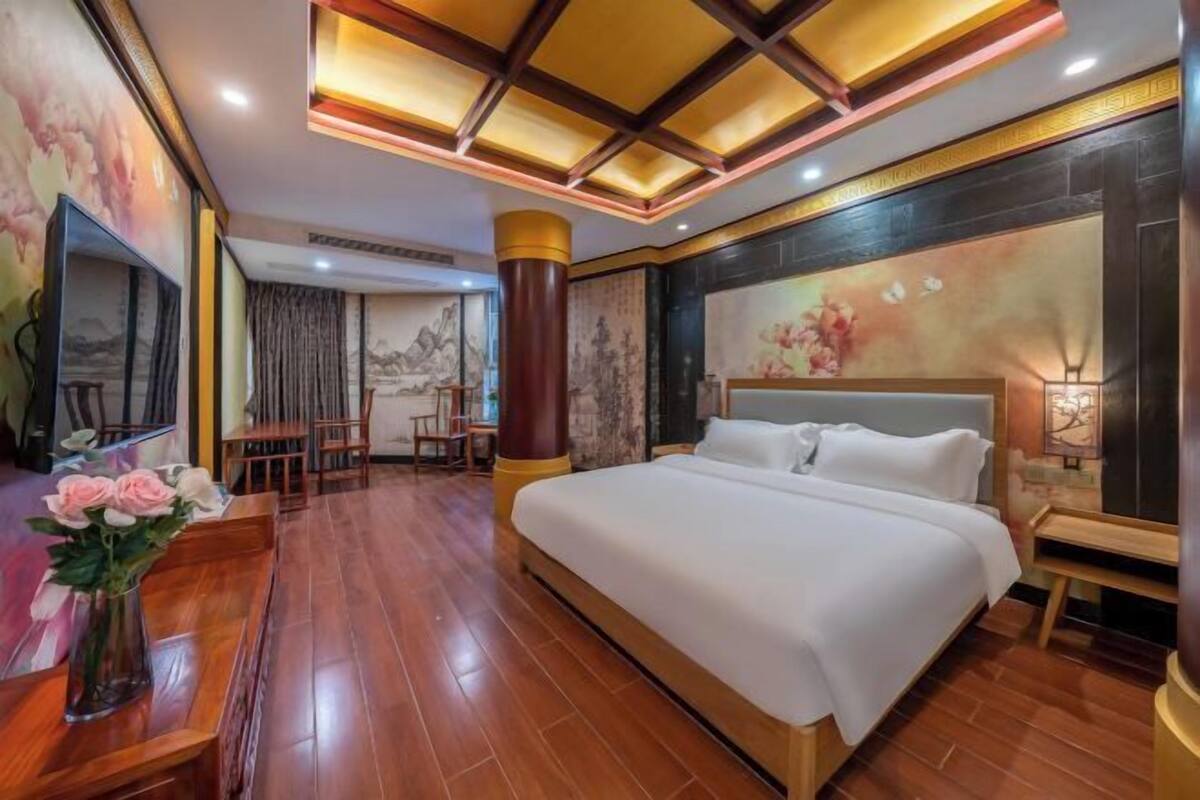 Ein Hotelzimmer mit einem großen Bett, Holzboden, einem Esstisch mit Stühlen und einer dekorativen Vase.