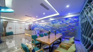 Un comedor moderno con una mesa de madera y sillas color turquesa, una pared decorativa con un mural de peces y una estantería con libros.
