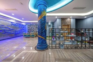 Un hall d’entrée avec une grande colonne bleue, un mur orné d’un motif lumineux bleu et un espace détente avec un banc.