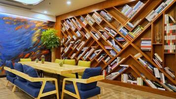 A room with a wooden bookshelf, a table with chairs, and a large painting on the wall.