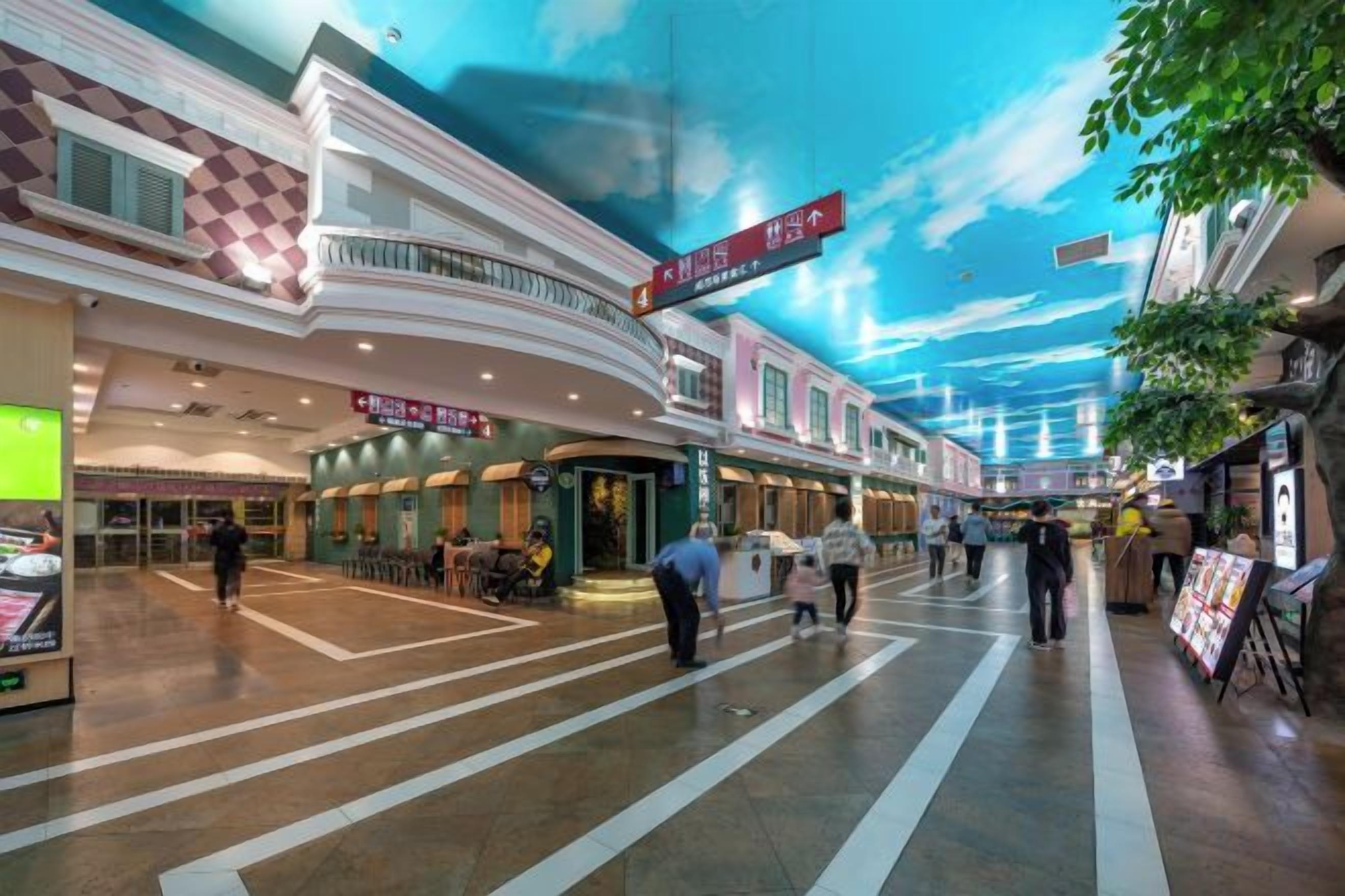 A shopping mall with a ceiling mural, indoor seating areas, and a variety of shops.