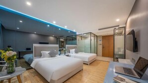 Une chambre d’hôtel moderne équipée de deux lits, d’un bureau avec un ordinateur portable et d’une cloison en verre.