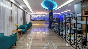 Un moderno vestíbulo de hotel con sofás turquesa, un mostrador de recepción y una columna iluminada en azul.