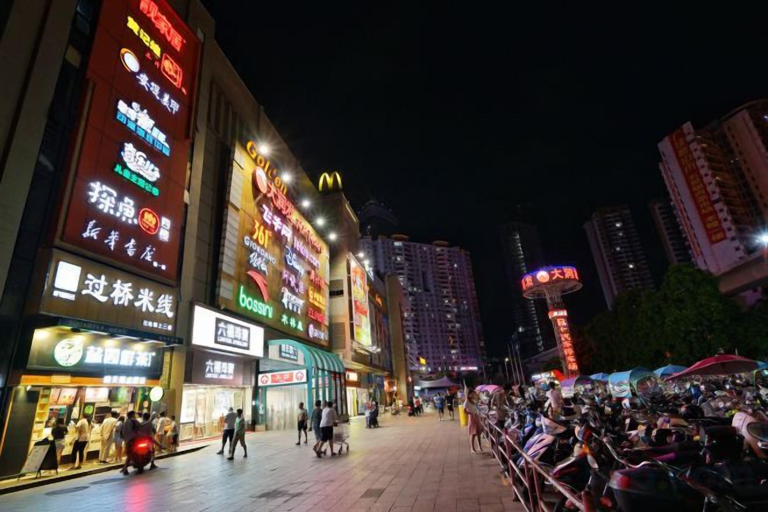 Une rue de la ville de nuit, avec des enseignes et des devantures de magasins illuminées.