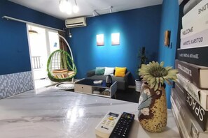 Una habitación con sofá, sillón colgante, mesa de centro y control remoto sobre una mesa de mármol.