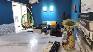 Una sala de estar moderna con una pared azul, un sofá con cojines, una silla colgante, una mesita de centro y un jarrón con una planta.