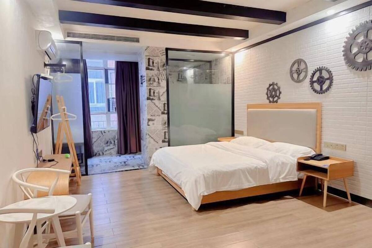 Ein modernes Schlafzimmer mit Bett, Schreibtisch und Stuhl. Ein Fenster mit Vorhängen, eine Wand mit dekorativen Zahnrädern und eine Tür zu einem anderen Raum.