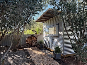Una petita cabana de fusta amb una finestra, envoltada d'oliveres i una tanca de làmina corrugada.