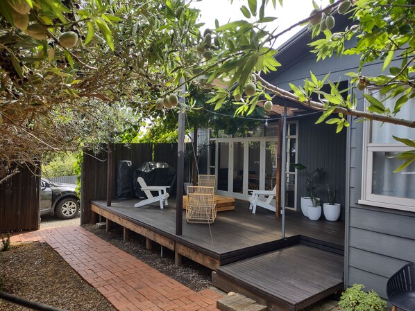 A covered patio with outdoor seating, a barbecue grill, and a vehicle in the background.