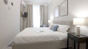 A hotel room with a large bed, a flat-screen TV, a bedside table with a lamp, and a window with curtains. - Easylife - Elegant apartment in Ostiense area (Roma)