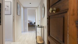 A hallway with a wooden door, a small table with a mirror, and framed pictures on the walls. - Easylife - Elegant apartment in Ostiense area (Roma)