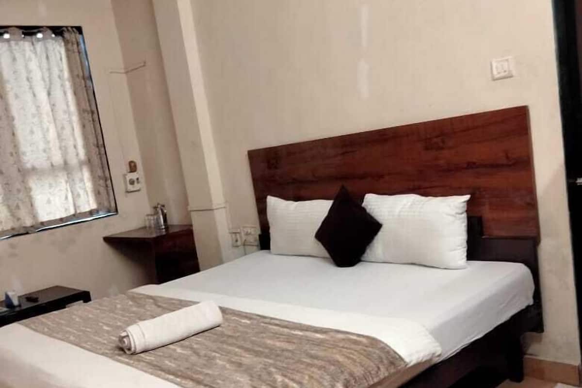 Uma cama bem arrumada com cabeceira de madeira, mesa de cabeceira com abajur e janela com cortinas.