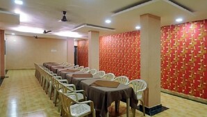 A conference room with rows of tables and chairs, a patterned wall, and ceiling fans.