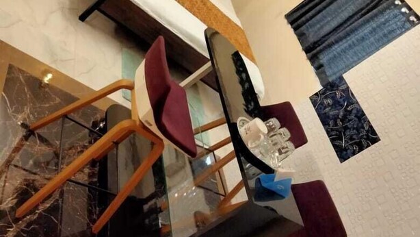 A modern hotel room with a bed, a glass table, and a seating area with chairs. - HOTEL SARIKA (Murbad)