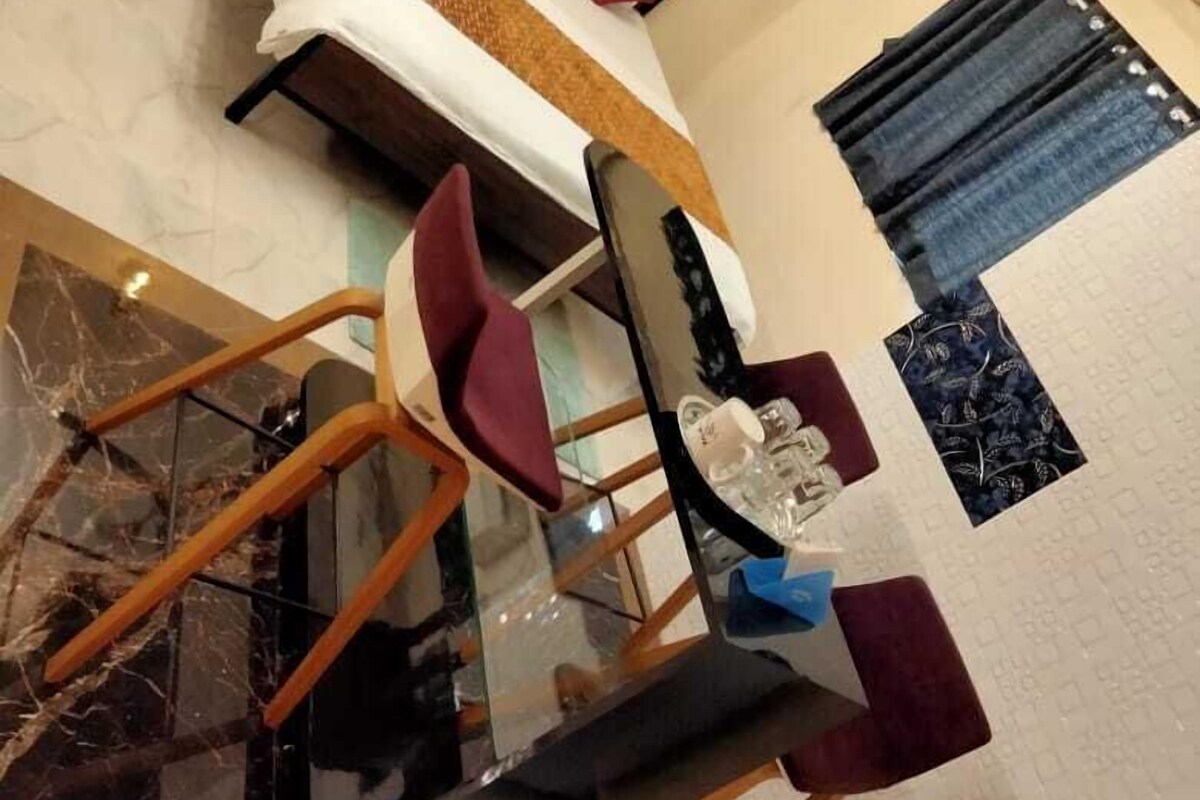 A modern hotel room with a bed, a glass table, and a seating area with chairs.
