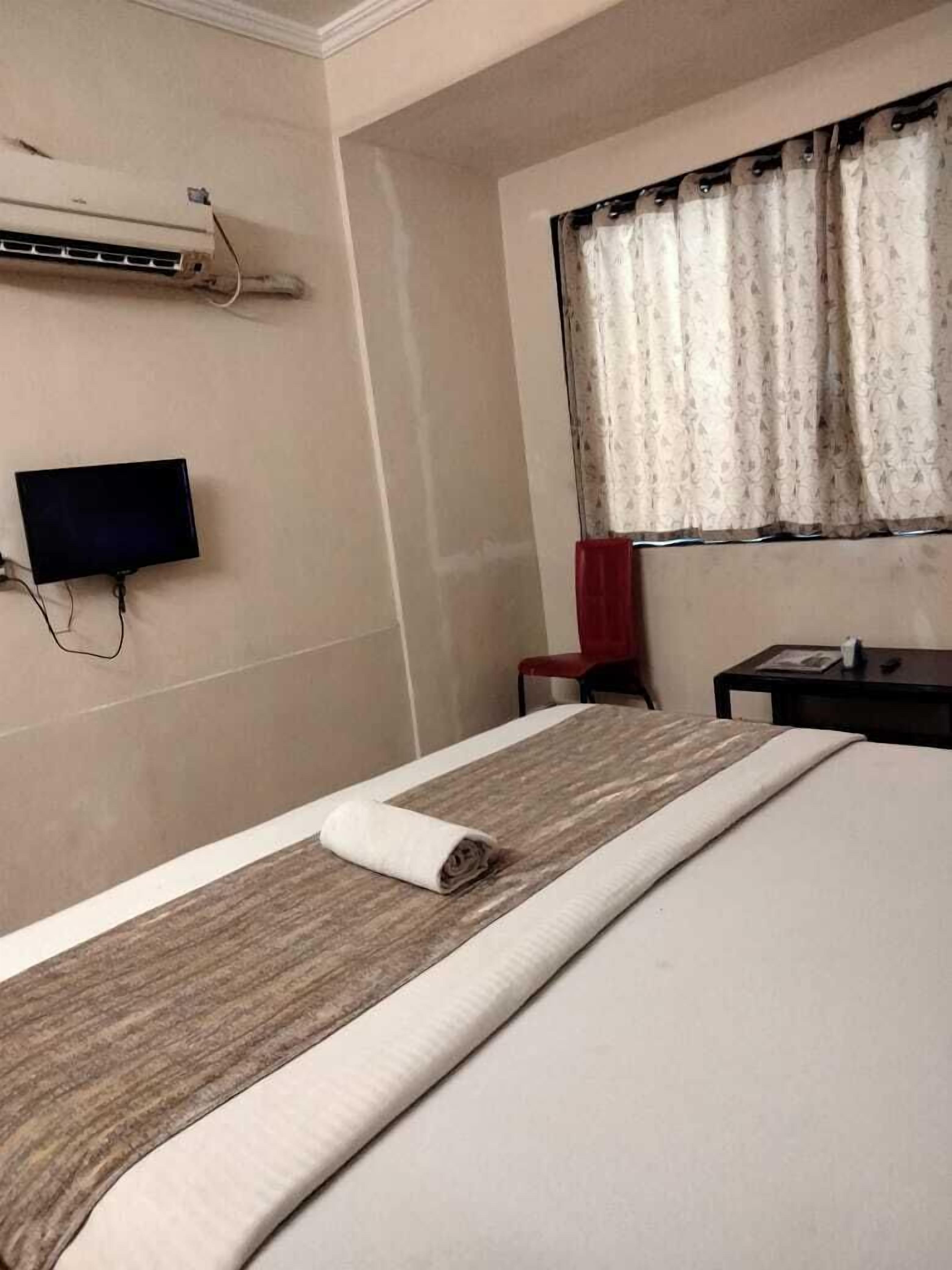 Habitación de hotel con cama, televisor de pantalla plana en la pared y ventana con cortinas.