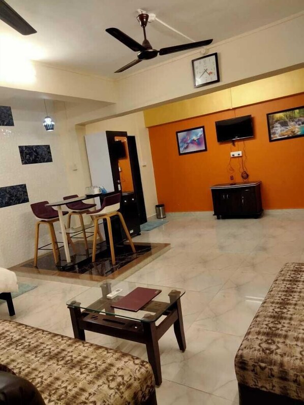 Ein Wohnzimmer mit Deckenventilator, Essbereich mit Stühlen und Tisch, einer Couch und einem an der Wand befestigten Fernseher.