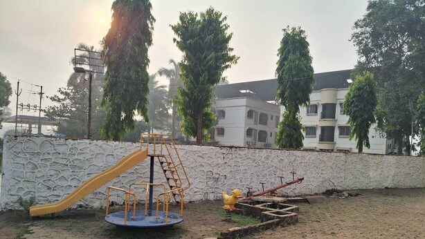 A playground with a slide and climbing structure, surrounded by a paved area and a stone wall.