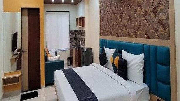 A hotel room with a bed, a TV, a bathroom, and a kitchen area. - HOTEL SARIKA (Murbad)