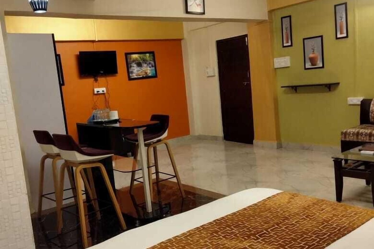 A living room with a sofa, a coffee table, and a TV mounted on the wall. There is a ceiling fan and a door leading to another room.