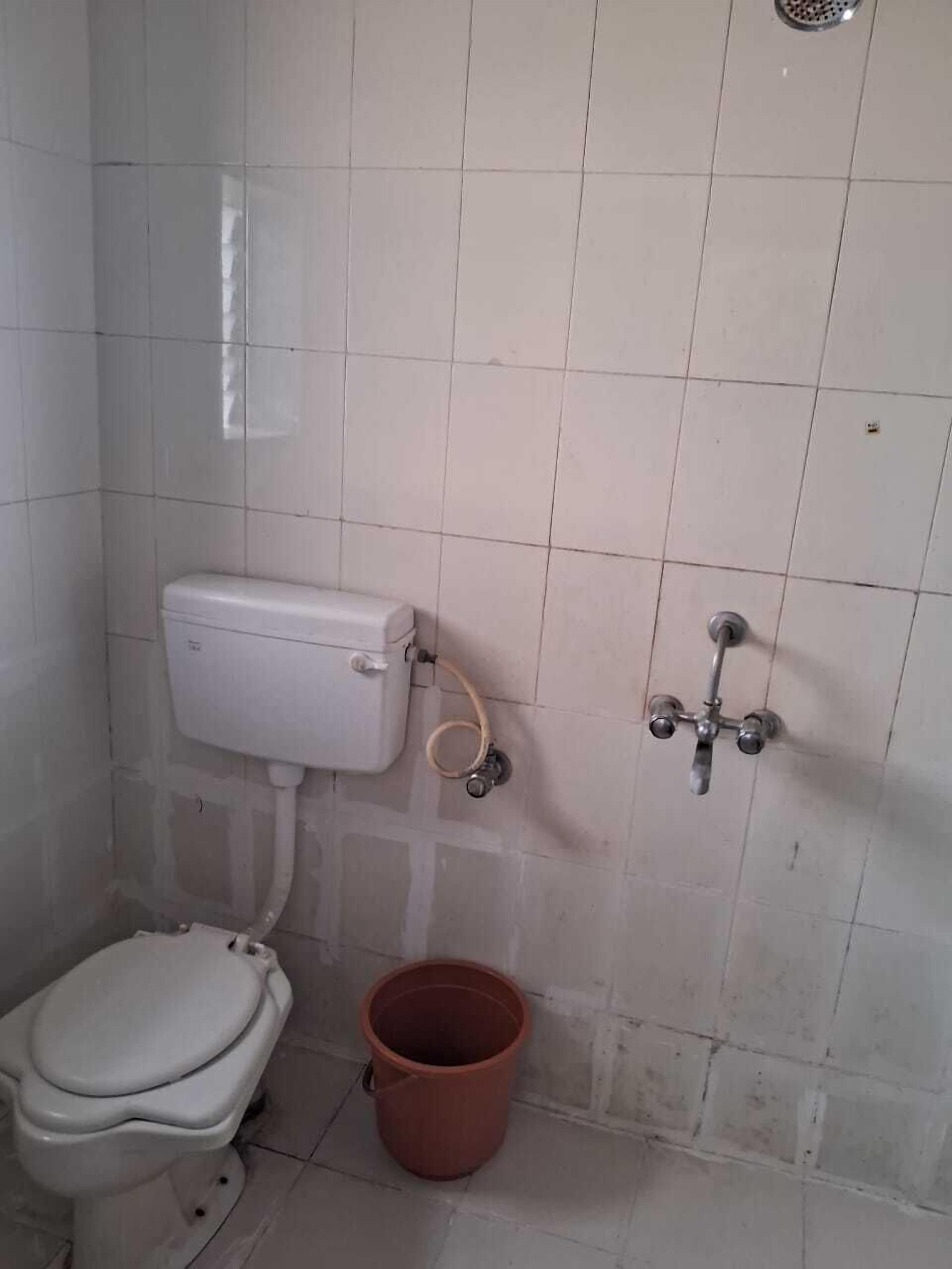 A small, tiled bathroom with a toilet, a bidet, and a bucket.