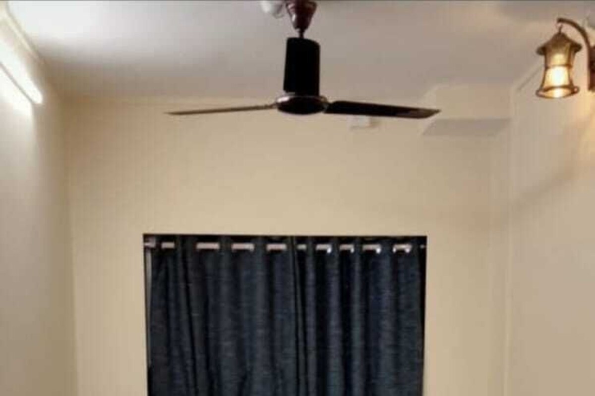 A bedroom with a wooden bed, dark curtains, a ceiling fan, and a bedside table.