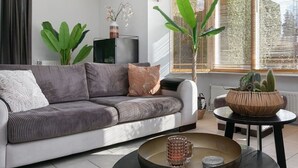 A modern living room with a sofa, a coffee table, and large windows with blinds. - Luxurious country house with whirlpool, sauna and private swimming pool (Schoonloo)