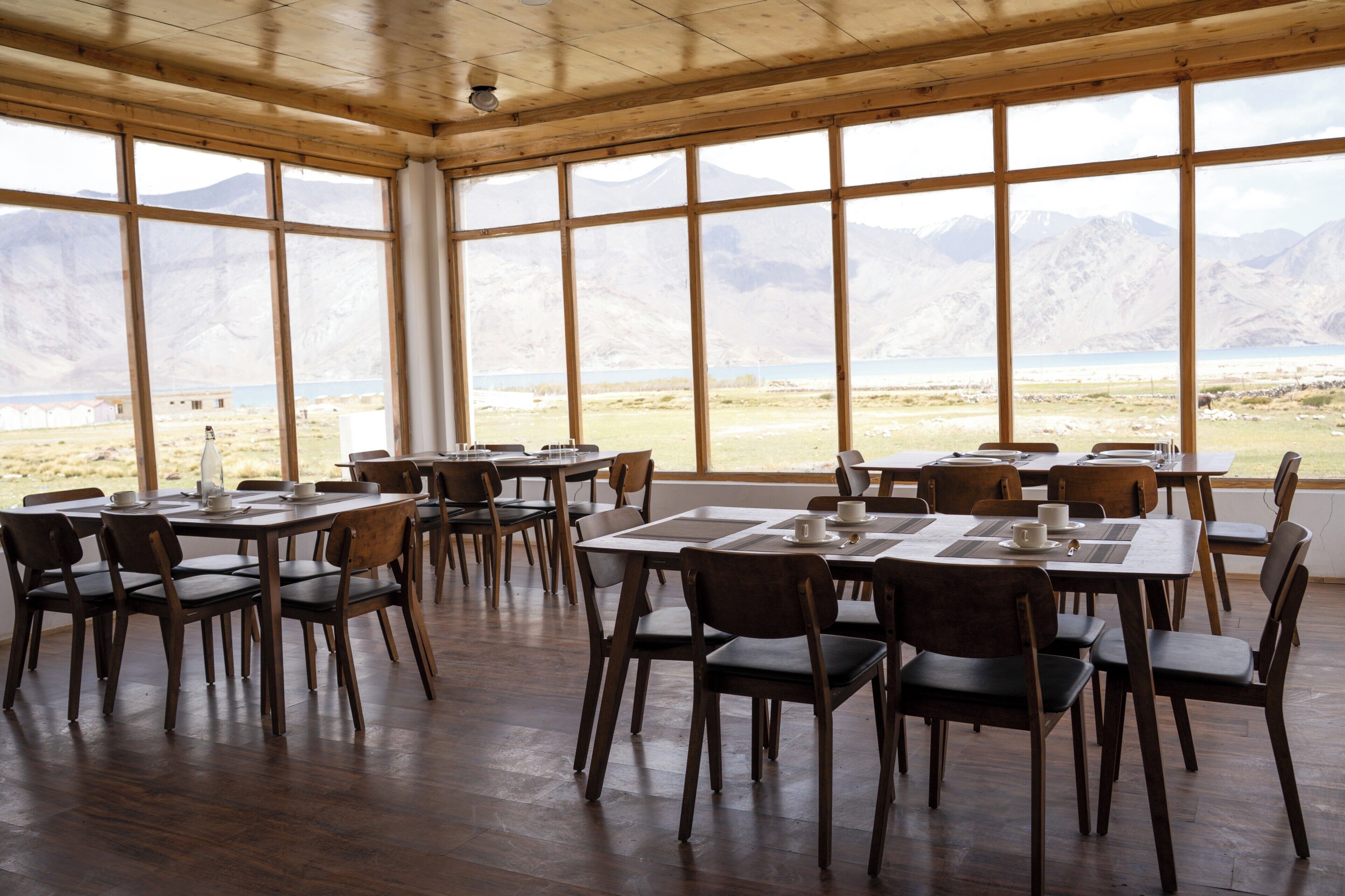 Un espace repas avec des tables et des chaises en bois, de grandes fenêtres offrant une vue sur les montagnes.