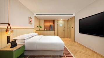 A modern hotel room with a bed, bedside table, TV, and a view into the room.