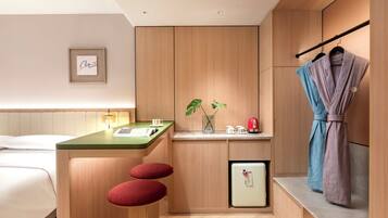 A modern hotel room with a wooden cabinet, a small kitchenette, a bed, and a robe hanging on a rack.