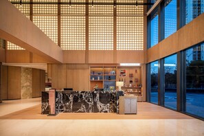 A modern hotel lobby with a reception desk, wooden paneling, and large windows offering views of the cityscape. - Atwell Suites Hefei City Center By IHG (Hefei)