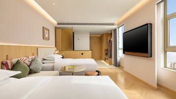 A modern hotel room with a large bed, a flat-screen TV mounted on the wall, and a view of the city through the window.