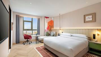 Habitación de hotel moderna con una cama grande, un escritorio con silla y vistas a la ciudad, con un paisaje urbano visible a través de la ventana.